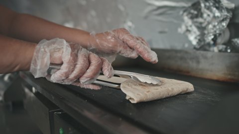 Close up of unrecognizable hands turning tacos while heating them up on professional pita oven at kitchen