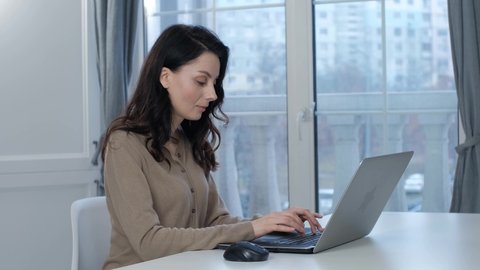 Freelancer writer woman communicating with client through internet. Free lancer worker working from home. Stock video of pretty brunette model in 30s typing text on laptop computer keyboard 
