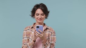 Happy charismatic fun young brunette woman 20s years old wears plaid shirt doing selfie shot on mobile phone post photo on social network isolated on pastel plain light blue background studio portrait