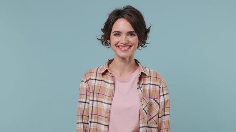 Happy charismatic young brunette woman 20s years old wears plaid shirt look camera do saluting gesture isolated on pastel plain light blue background studio portrait. People emotions lifestyle concept