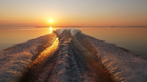 Beautiful view from running boat, saturated sunset and calm Ladoga, the wave from powerful motor cuts smooth surface of the lake water. Camera look back to Mantsinsaari Island from racing motorboat