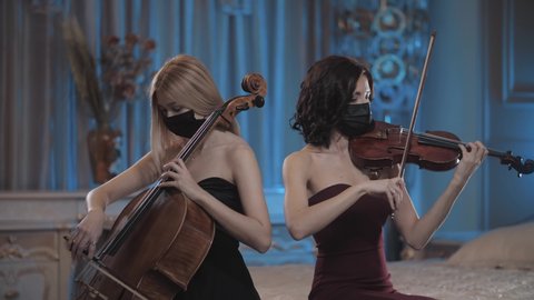 cute girls in mask play in a beautiful room. violin and cello. repetition . duet of musicians. Pandemic