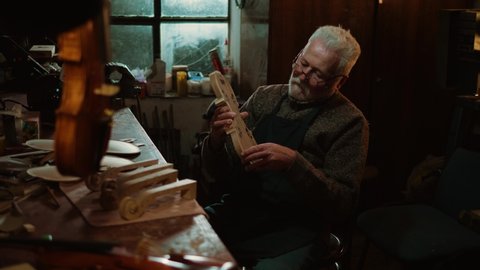 Late in the evening, a retired old craftsman makes handmade violins in his workshop.