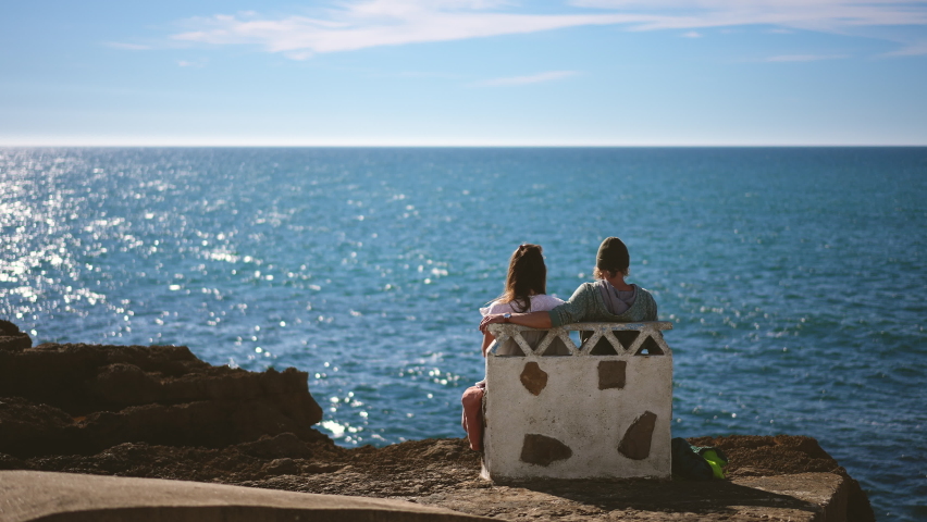 Tourism, scenery view at European Portuguese town of Ericeira. Young tourist people at sea. Travelers family sitting on stone bench by ocean. Lovely couple sea sights in Europe for traveling person. Royalty-Free Stock Footage #1084038892
