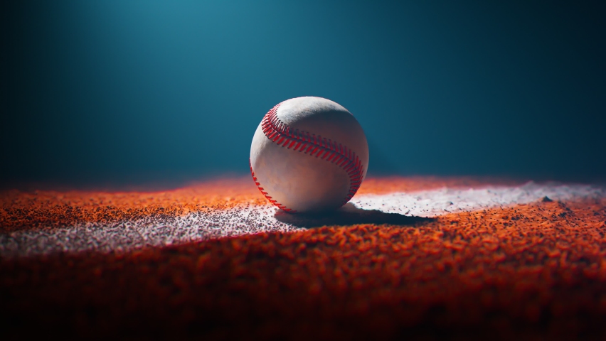 Baseball lying on a white field line painted on the orange dirt. Dark stadium with a single spotlight illuminating the ball. National American sports equipment on the ground. Camera rotates around it.