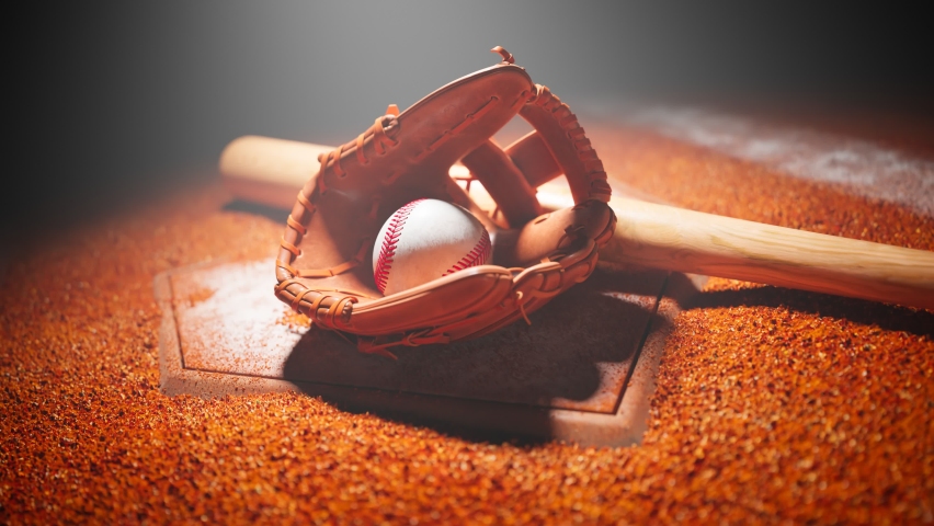 Baseball leather glove, ball and bat on a dirty white base in the spotlight. Dark stadium with orange gravel dirt and white base lines visible. National american sport equipment on the ground.