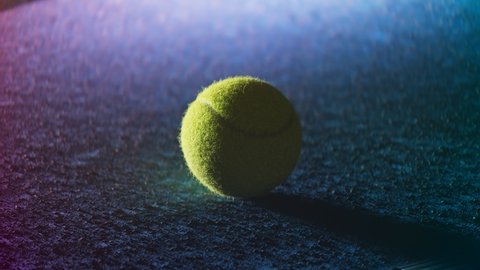 Camera rotates around one tennis ball on an empty court. Night shot with backlighted ball with blue and pink light behind. Sport and leisure equipment.