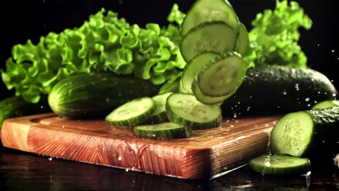 Pieces of cucumber fall on a cutting board with splashes of water. On a black background. Filmed is slow motion 1000 fps. High quality FullHD footage