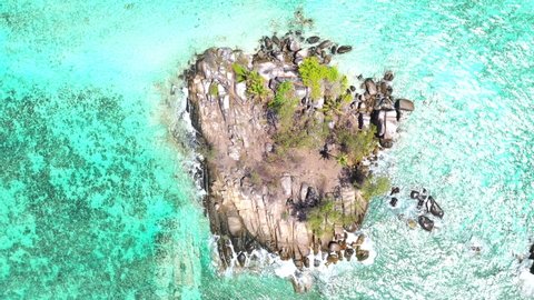 Drone clip with a view of a mini island on Mahe with turquoise blue water, rocks and palm trees in the Seychelles 