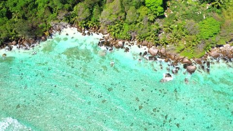 Drone clip with a view from above of the rocky beach at Anse Marie-Louise in Mahe with turquoise blue water and palm trees in the Seychelles 