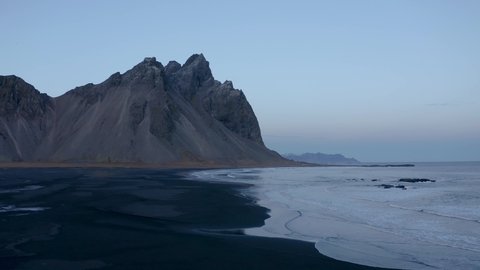 Aerial forward flight over volcanic black beach and Vestrahorn Mountain in background - Early morning on Iceland Island