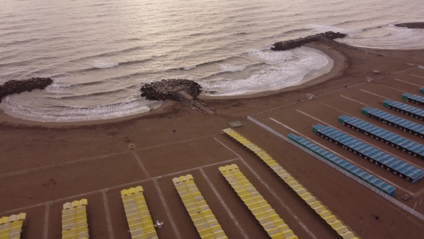 Aerial orbit shot of yellow and blue tents of spa resort at sandy beach during sunlight - Waves of Ocean reaching shore - Mar del Plata,Argentina