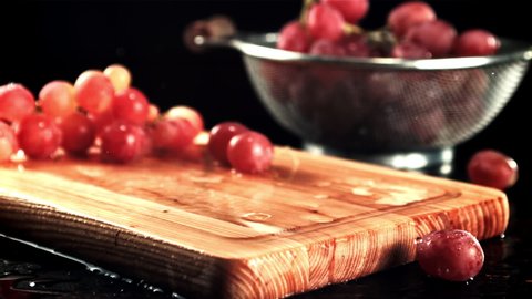 Grapes fall on a cutting board with splashes of water. On a black background. Filmed is slow motion 1000 fps. High quality FullHD footage