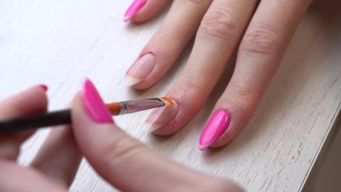 Applying a base coat before coating nails with nail polish. Selfmade manicure service. Manicurist paints nails with pink gel polish. Manicured pink nails. Nail polish application.