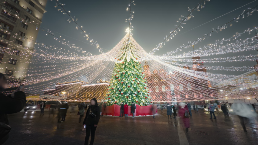 Camera moving around beautifully decorated Christmas tree with shiny garlands on the street of Moscow. People walking under atmospheric New Year illumination in motion timelapse.