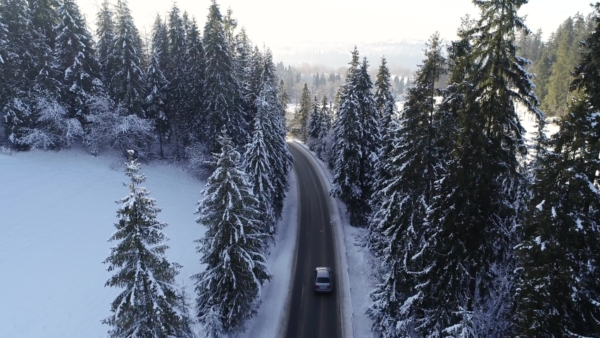 Aerial view of mountain twisted road in the winter and driving car. Epic, snowy white winter and snow capped forest. Road through frozen forest and luxury sedan. Royalty-Free Stock Footage #1084053142