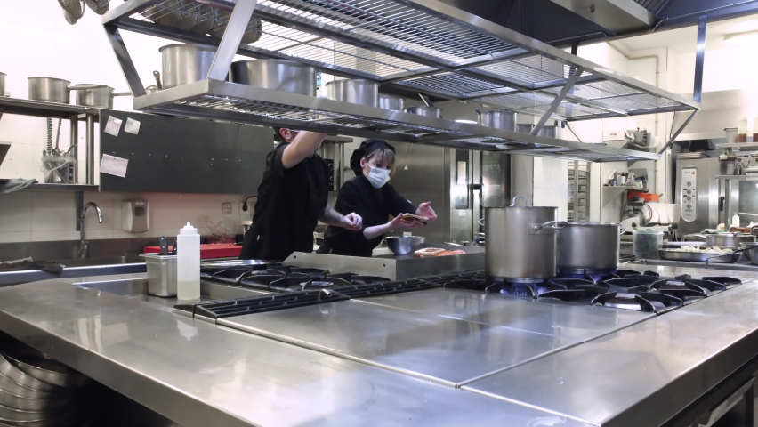 Group of chefs cooking together in the kitchen at restaurant wearing protective medical mask in coronavirus new normal concept. High quality 4k footage | Shutterstock HD Video #1084053835