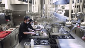 group of chefs cooking together in the kitchen at restaurant wearing protective medical mask in coronavirus new normal concept. High quality 4k footage - Powered by Shutterstock - Get 15% off with code: PIKWIZARD15