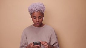 Cheerful young African American woman giggles and covers mouth looking at phone. Attractive ethnic female trying to hold back laughter by reading messages on smartphone or watching funny video