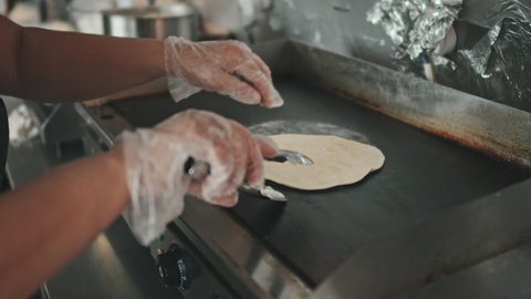 Close up of unrecognizable hands turning taco shell while heating it on open pita oven in kitchen