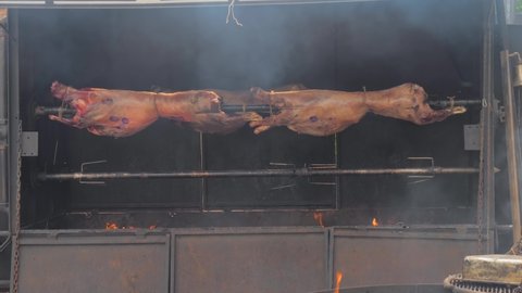 Process of cooking two roasted whole ram carcasses on spit at summer outdoor food festival, market - front view. Preparation, cookery, gastronomy and street food concept