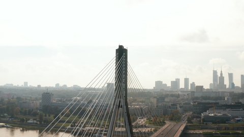 Fly around top of tall bridge pillar. Revealing cable stayed bridge over river and skyline with skyscrapers. Warsaw, Poland