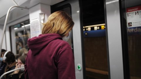 Woman standing in front of the door, get out underground carriage. Student gets off at station.