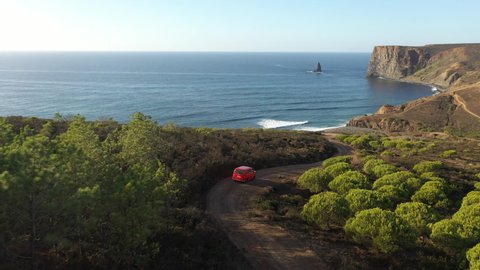 Red car driving over a dirt road to the sea