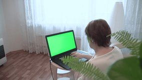 An adult woman with a laptop. An adult woman on the Internet. A laptop with a green chromakey in a woman's hand. Green background