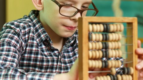 Portrait of a Caucasian schoolboy 7-8 years old wearing glasses counting on wooden abacus. The topic of education and learning mathematics. The child learns from the abacus. Selective focus