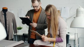 Young female fashion designer is talking to male colleague using tablet working in studio together. Small business and dressmaking concept. - Powered by Shutterstock - Get 15% off with code: PIKWIZARD15