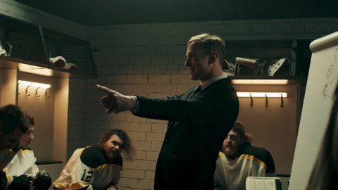 Happy cheerful talking to professional ice hockey team players on the locker room during the intermission. Motivation speech. Shoot with 2x anamorphic lens