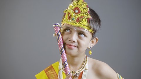 little Krishna thinking by holding flute in hand on gray background during shri krishna Janmashtami.
