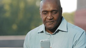 Elderly African american man holding smartphone looking at screen during video chat emotionally talks shares news with interlocutor, agrees says yes, surprised, refuses shows no case gesture by hand