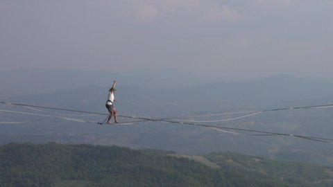 Castelnovo nè Monti, Reggio Emilia, Italy - 09.20.2021: Video of a tightrope walker on the slackline 200 meters above the precipice of the Bismantova stone. Equilibrium and balance concept