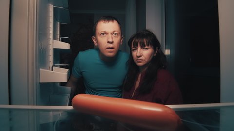 hungry man and woman open the refrigerator at night and take a sausage, night zombie