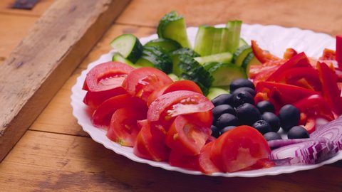 Ingredients for Greek salad on a plate. Fresh vegetables, feta cheese and olives for a summer salad. Camera movement over the table