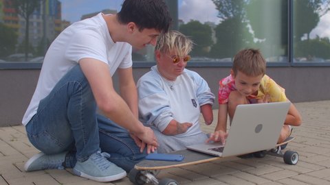 CZ, Kladno, Armenska, 4.8.2021. Disabled person with congenital malformations of the upper and lower endpoints surrounded by friends using the laptop. Outdoor lifestyle.