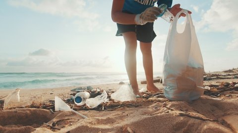 Young Caucasian woman environmental activist volunteers cleaning beach from non-degradable plastic waste saving world's oceans from pollution walks on sea sand at low tide. Caring for nature concept