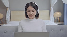 Happy young woman wear wireless headphones make video call online chat look at laptop screen sit on sofa, smiling girl talk to webcam communicate by internet computer conference app at home.