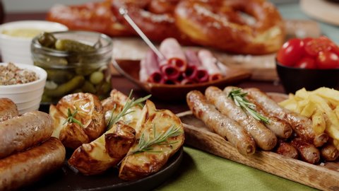 Traditional German Cuisine. Putting tray with smoked sasuages and fried potatoes, pickled cucumbers, bratwursts and fresh pretzels on table. Composition of Cooked National Czech Food. 