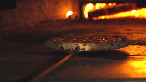 Pizzaiolo is putting pizza in the wood-fired oven. The pizza is cooking in the oven. The salami pizza is going into the oven. Chef putting pizza with a shovel into the wood-fired oven. Slow motion