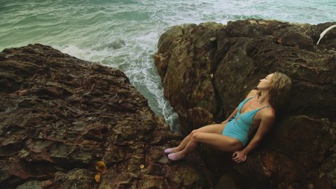 Woman meditates, relaxes on rock crack reef hill in stormy morning cloudy sea. Concept feminine, sexual vaginal health, womanly, freedom, freshness