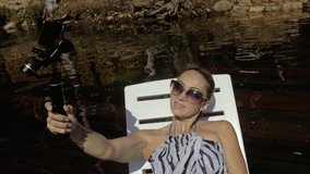 Woman shooting on handheld film gimbal stabilization for smartphone. Girl lie sunbed on pier make selfie. Blogger broadcast video vlogging.