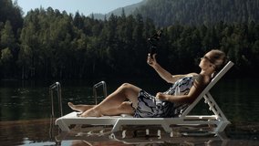 Woman shooting on handheld film gimbal stabilization for smartphone. Girl lie sunbed on pier make selfie. Blogger broadcast video vlogging.