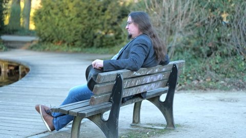 [4k] long haired man sitting on park bench playing with his hat