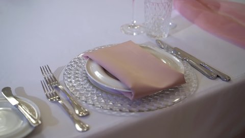 Served table in a restaurant for dinner, lunch or celebration. White tablecloth, plates, pink napkin and glasses. Holiday indoors. Empty with no people and food. Decorated for wedding