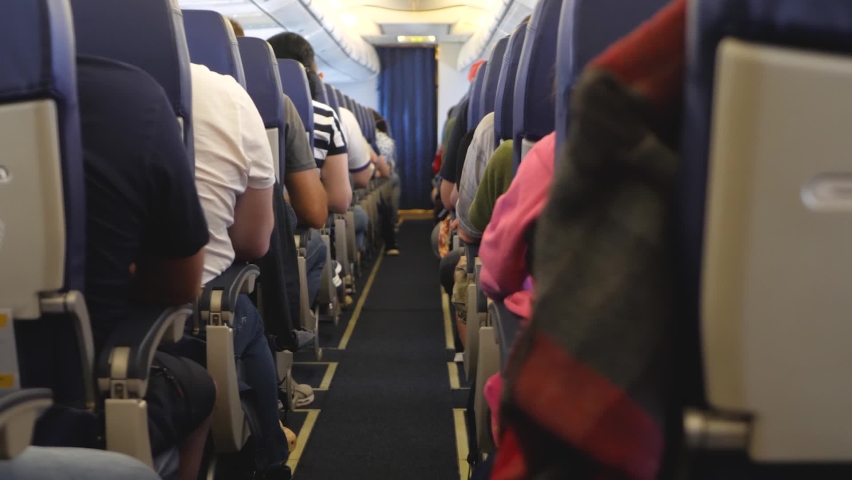 Passengers sits inside airplane. Narrow aircraft cabin. People travels. Jet plane interior view with unrecognizable passengers in comfortable seats of aircraft Royalty-Free Stock Footage #1084111495