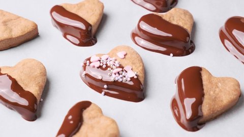 Cooking heart cookies glazed in chocolate and pink sprinkles on white background. Valentine day concept.