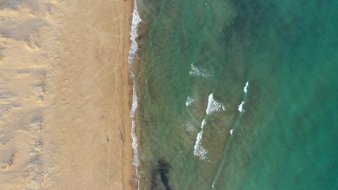 Tropical beach aerial view, Top view of waves break on tropical yellow sand beach. Sea waves seamless loop on the beautiful sand beach. Beautiful tropical beach aerial, bird's eye view of ocean waves.